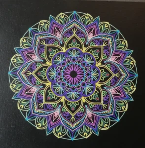 "Mandala coloré peint à la main sur fond noir, présentant des motifs géométriques complexes et symétriques dans des tons de violet, bleu, jaune et vert."