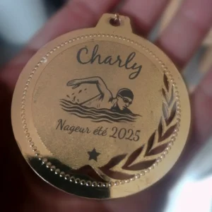 Médaille dorée gravée avec prénom 'Charly', illustration d'un nageur et texte 'Nageur été 2025', cadeau personnalisé