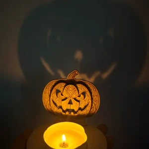 Photophore citrouille d'Halloween ajouré en bois gravé au laser avec une bougie allumée projetant des ombres sur un mur.