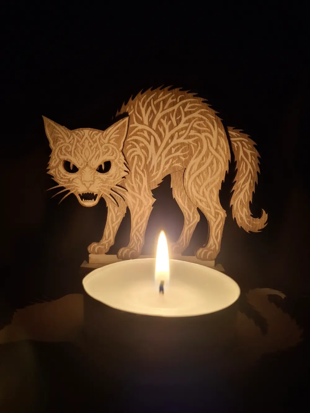 Photophore chat 2 d'Halloween ajouré en bois gravé au laser avec une bougie allumée projetant des ombres sur un mur.
