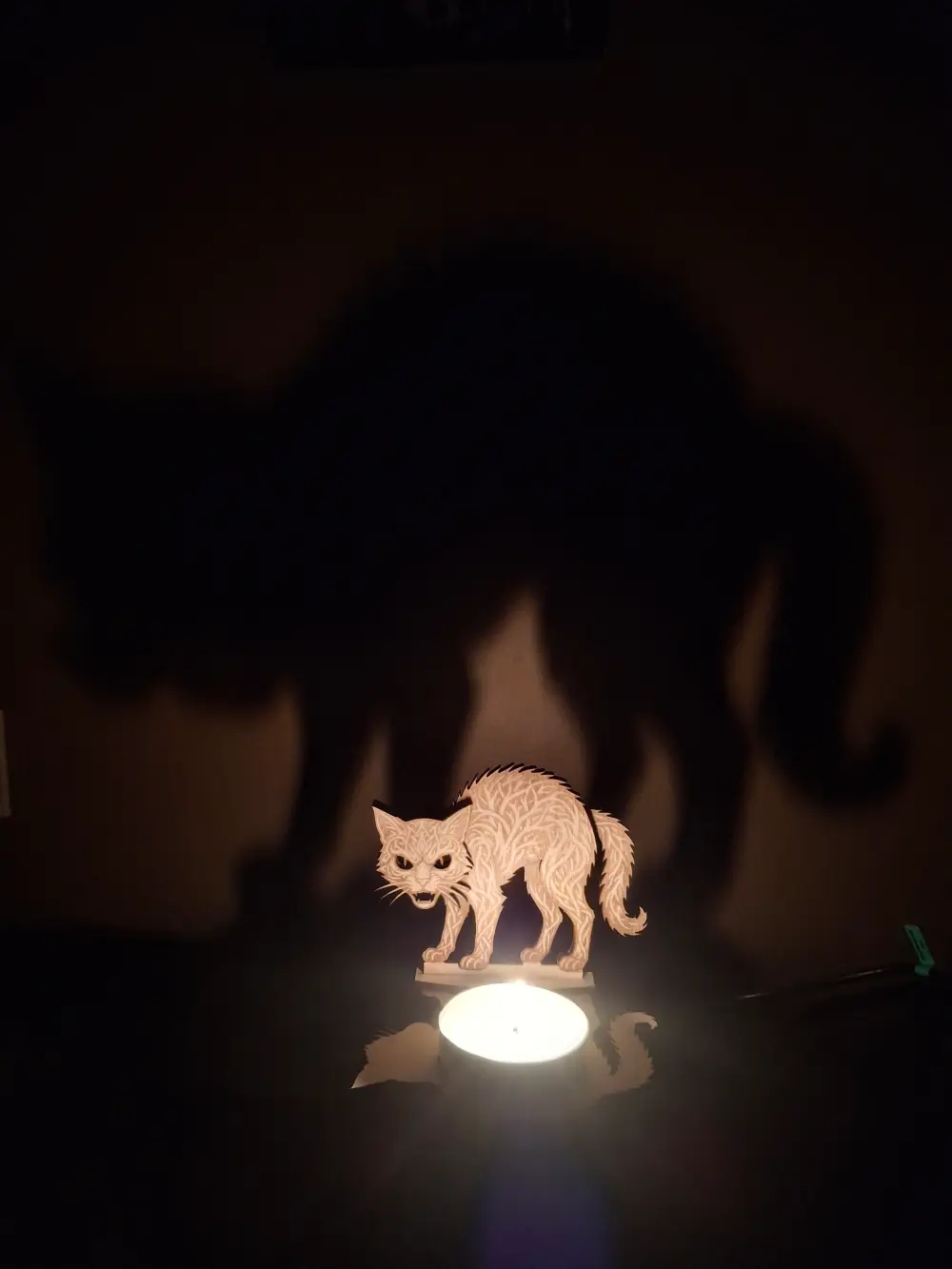 Photophore chat d'Halloween ajouré en bois gravé au laser avec une bougie allumée projetant des ombres sur un mur.